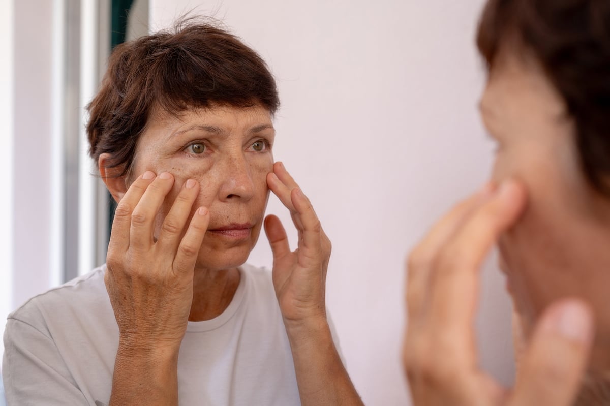 Mature woman examining puffiness and under-eye bags in the mirror