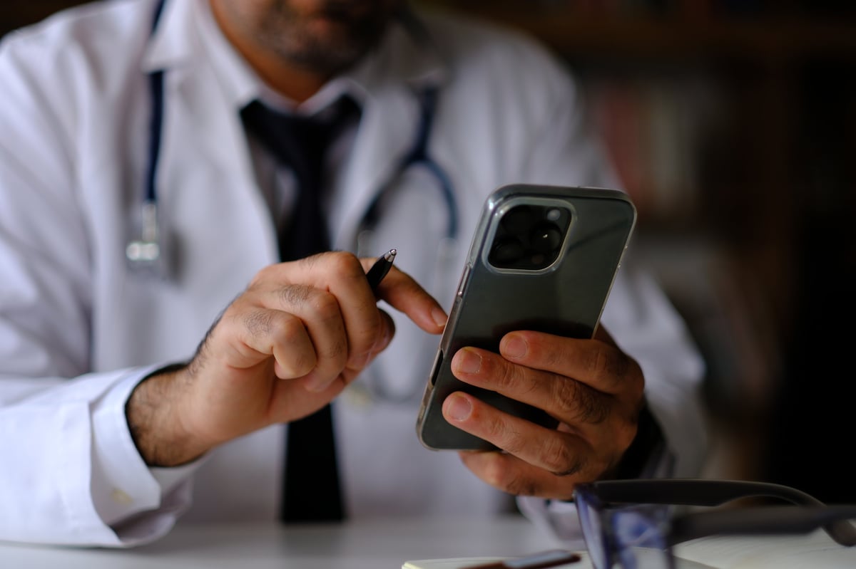 Doctor que maneja su presencia digital con su teléfono inteligente en la consulta