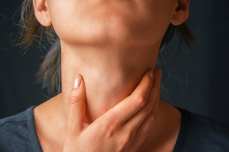 Woman touching her throat with hand against dark background, examining neck area for pain or swelling